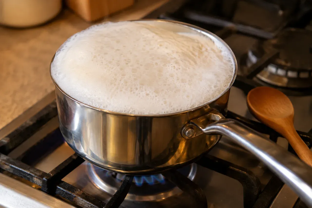 Casserole de lait sur une gazinière, la mousse montant jusqu'au bord, avec une cuillère en bois posée sur le côté